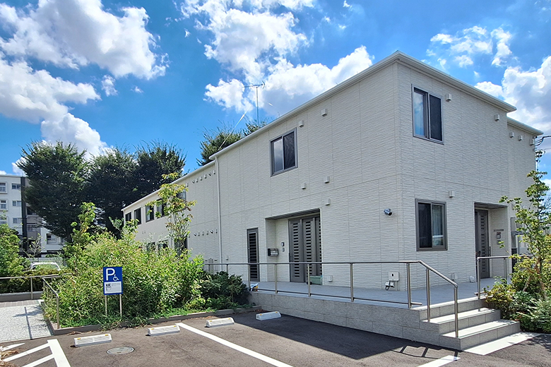 日中サービス支援型グループホーム「ユースタイルホーム」の外観。白い建物が青空と緑の木々に囲まれて建っている様子が見受けられる。