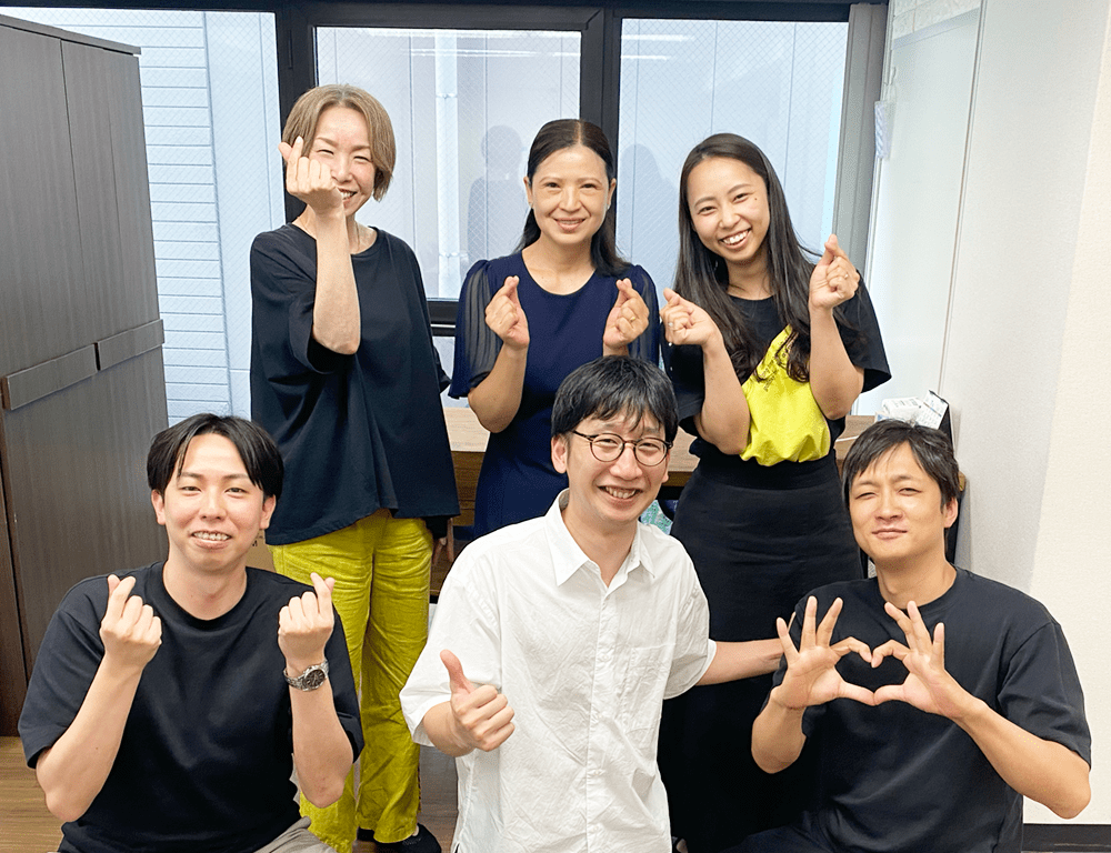 ユースタイルラボラトリー株式会社のスタッフがポーズを決めているグループ写真。各メンバーが手でハートやサムズアップのジェスチャーをしている。